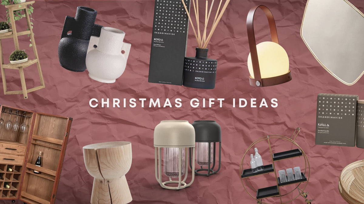 Christmas gift ideas featuring designer homewares including sculptural vases, Scandinavian candles and diffusers, portable lamps, mirrors, timber furniture and a bar trolley on a textured blush background.