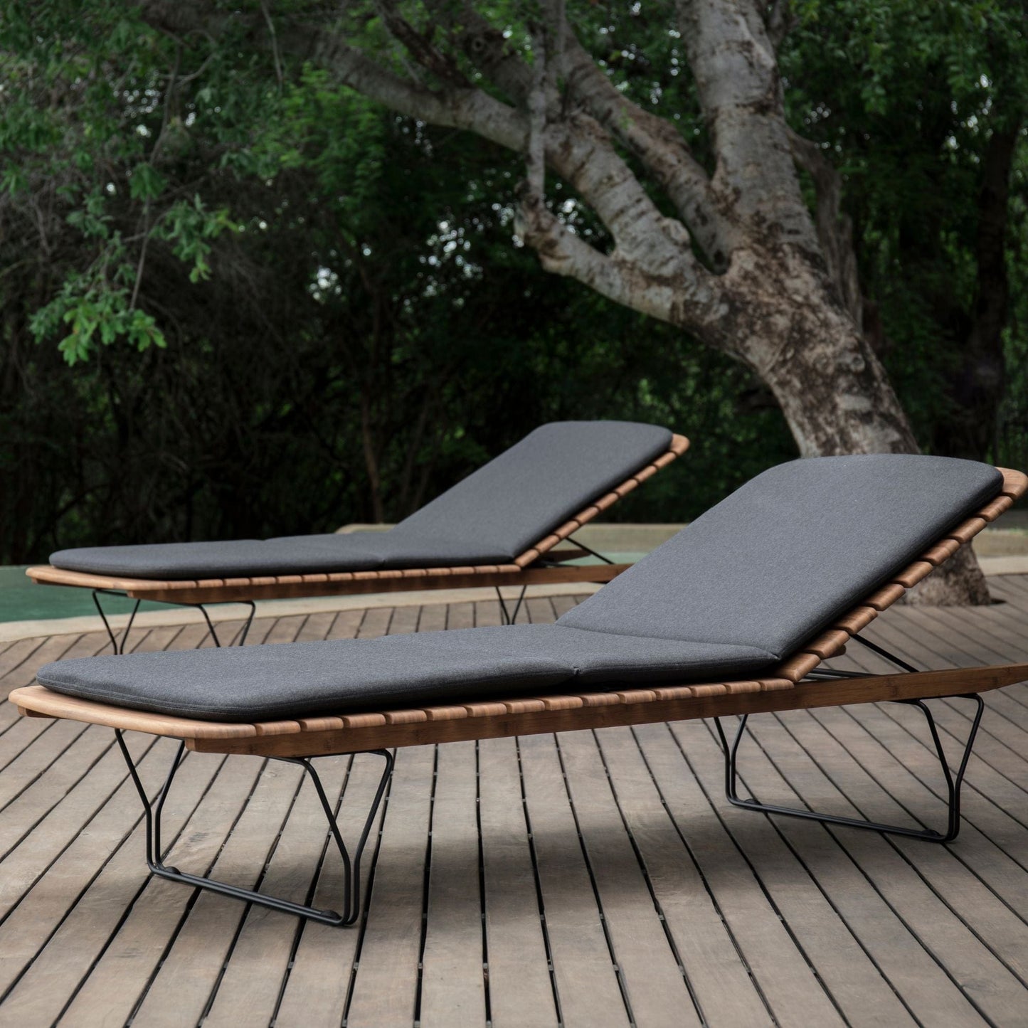 Two outdoor chaise lounge chairs on a wooden deck.