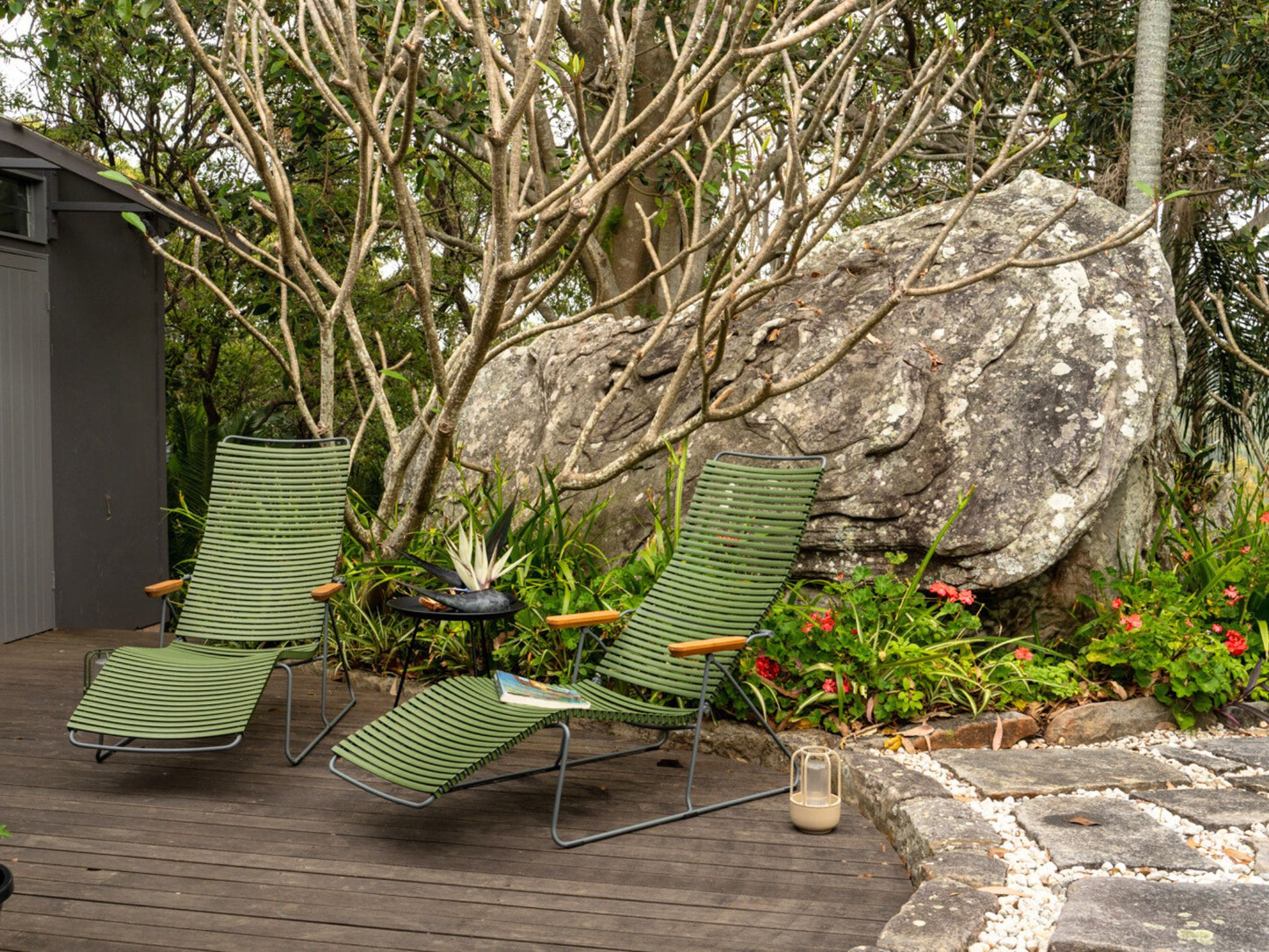 Two green lounge chairs on a wooden deck near a large rock.