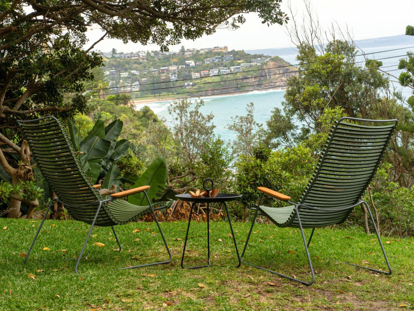 Two green lawn chairs and small table overlooking ocean.