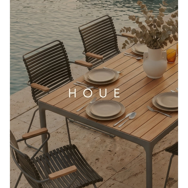 Outdoor dining set with table and chairs by a body of water, featuring the brand 'HOUE'.