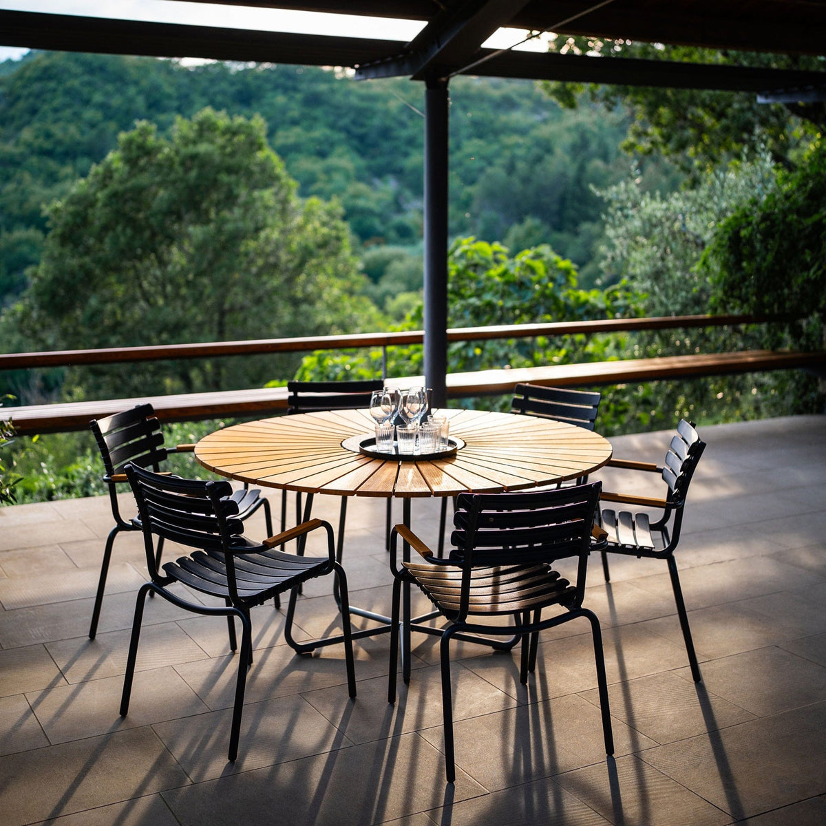 Circle dining table with chairs on a patio overlooking a forest.