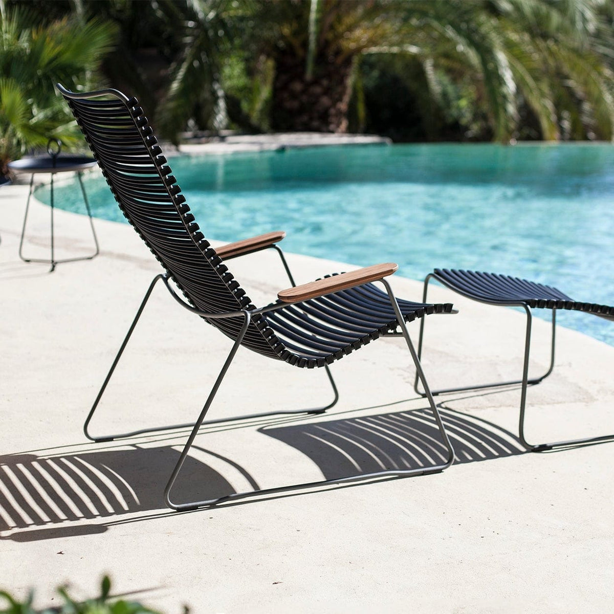 Ergonomic black outdoor lounge chair placed next to a pool with a footrest in front