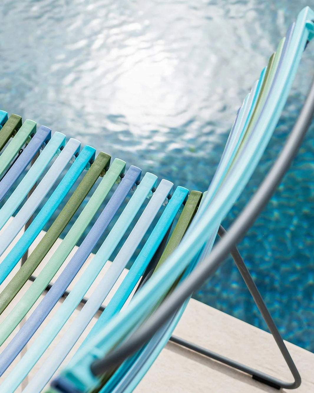 Colorful striped chair by a pool with clear blue water.
