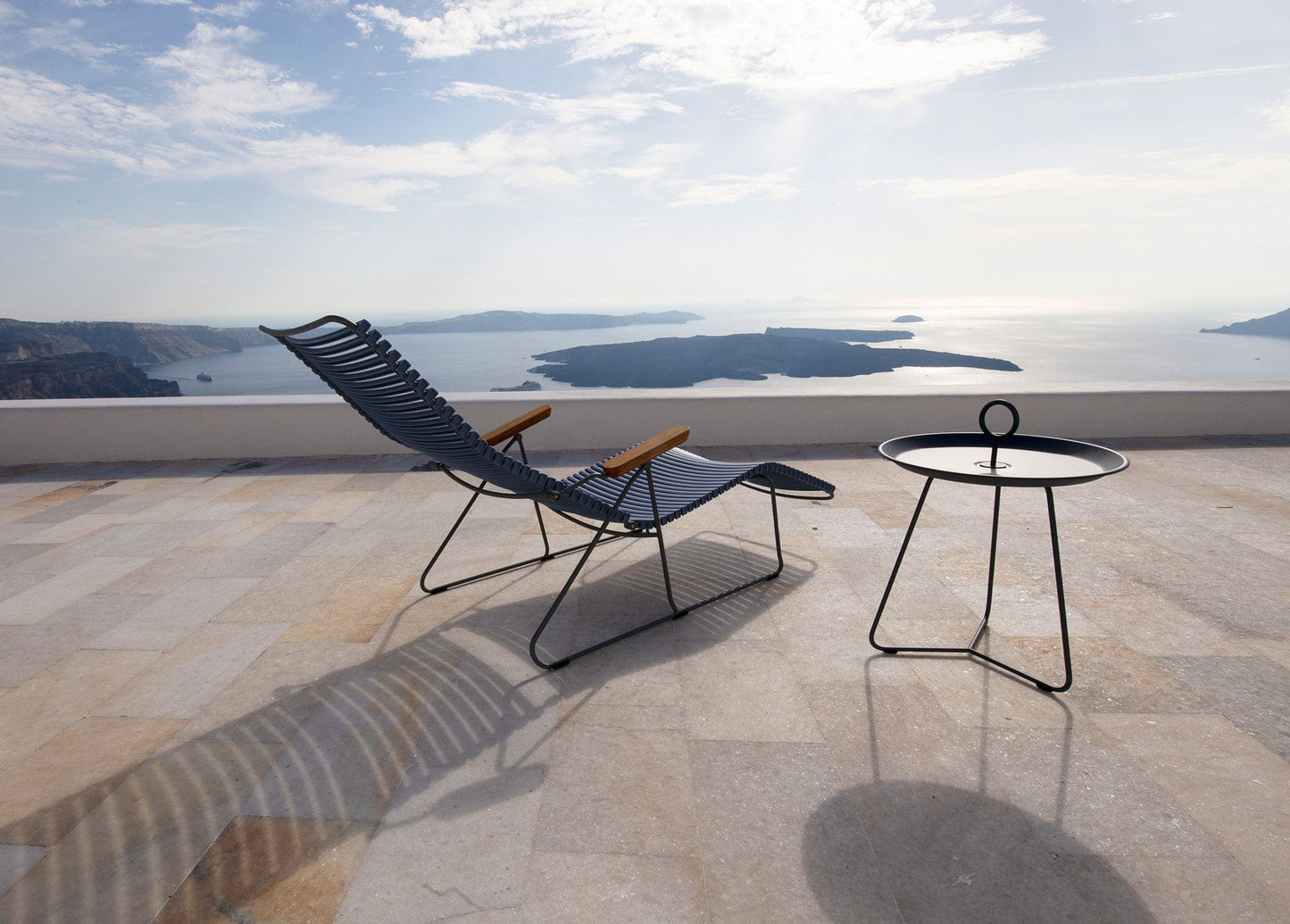 Black HOUE CLICK sunlounger and side table on a terrace overlooking the sea.