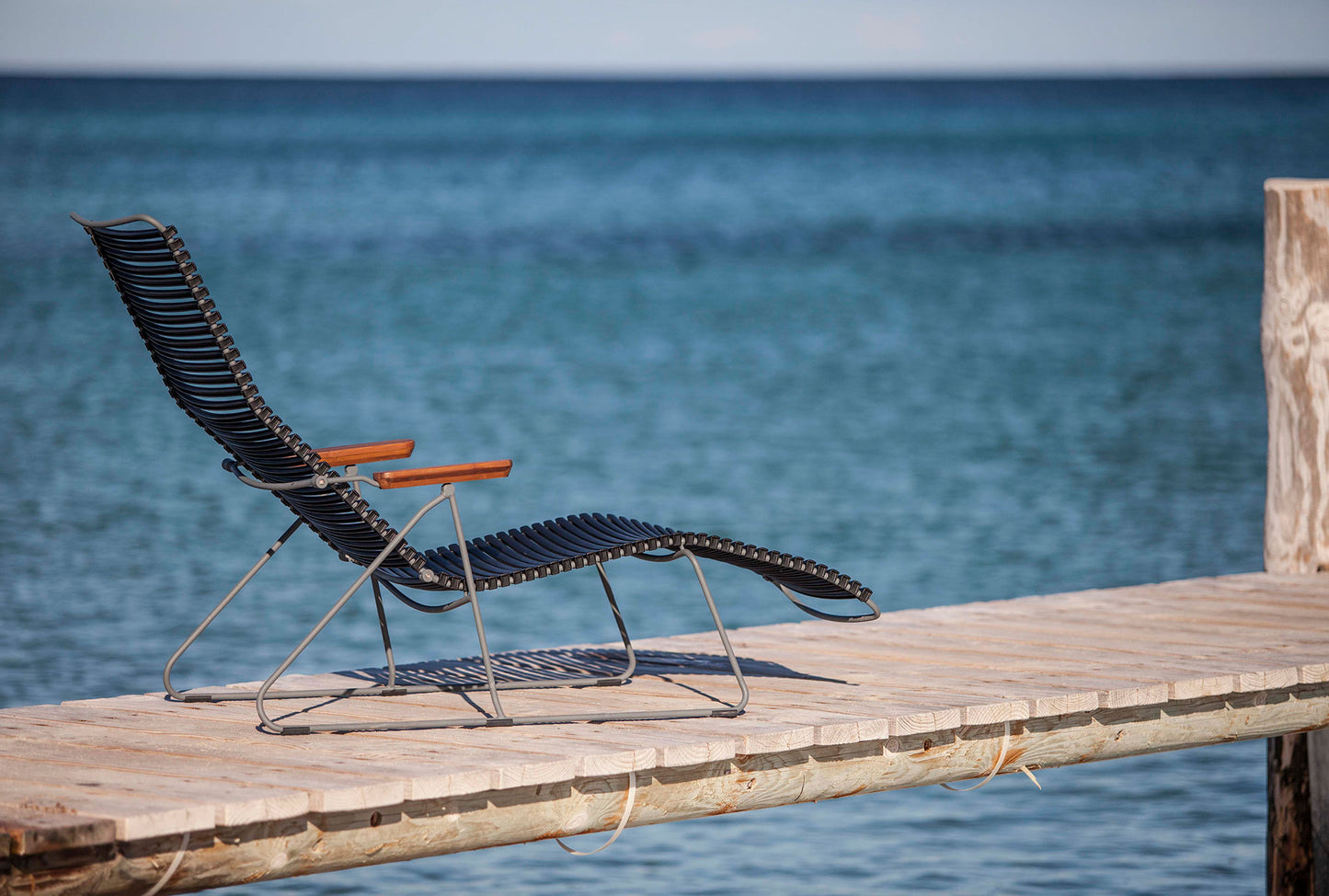 Black HOUE CLICK sunlounger on a pier overlooking the ocean.