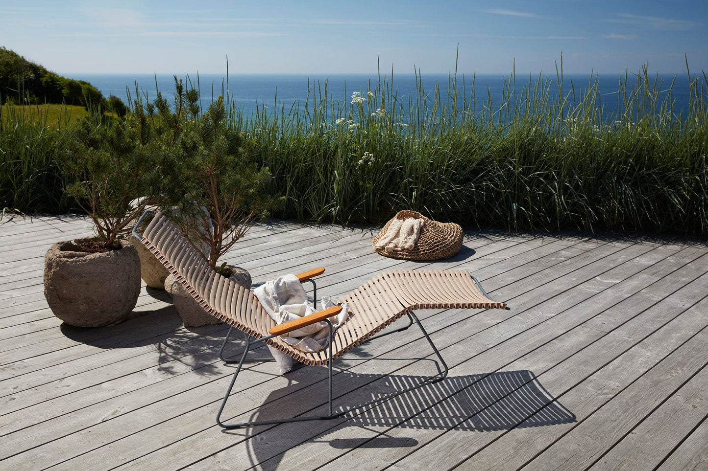 CLICK Sunrocker sand HOUE chaise lounge on a wooden deck overlooking the ocean.