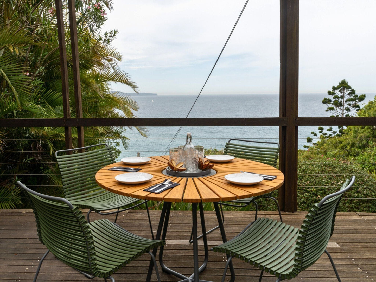 Circle table and green click chairs on deck overlooking ocean
