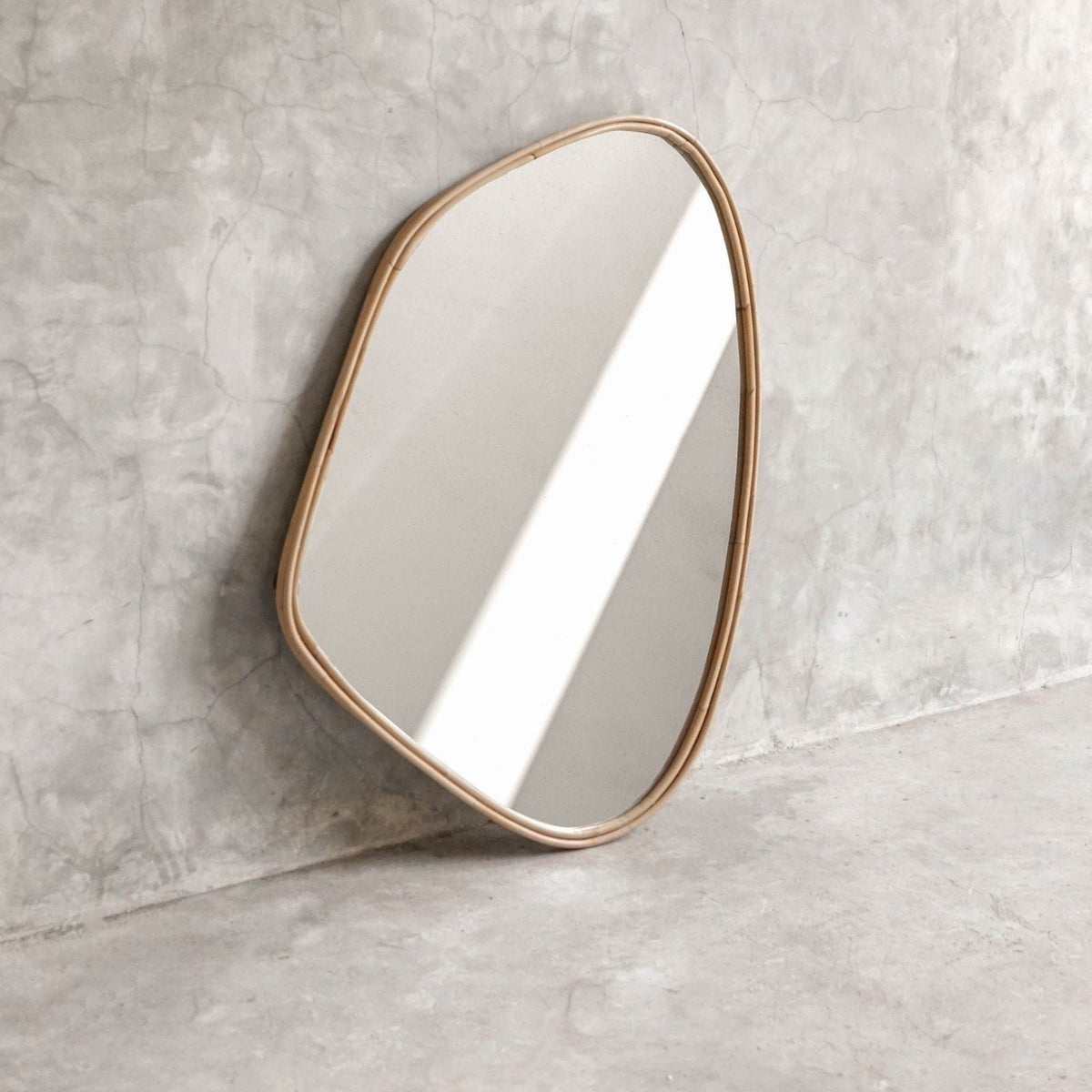 ELE125 Mirror with organic shape and gold frame against concrete wall.