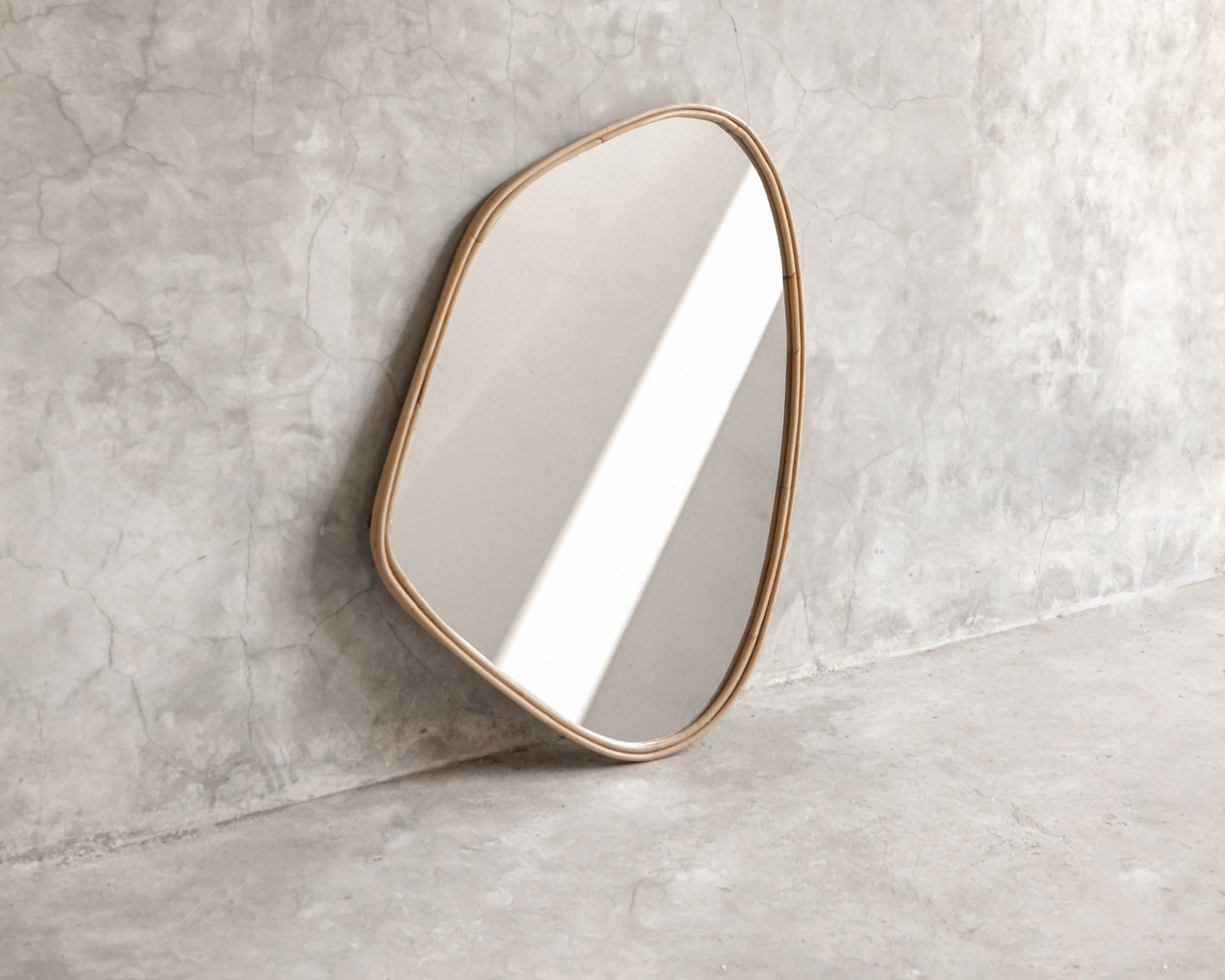 ELE125 Mirror with organic shape and gold frame against concrete wall.