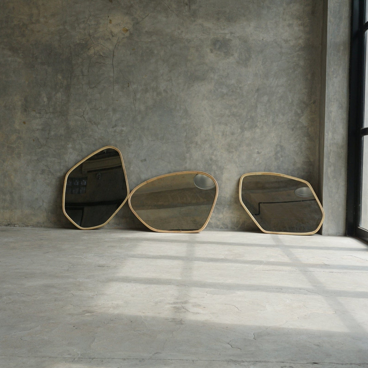 Three abstract mirrors leaning against a gray wall