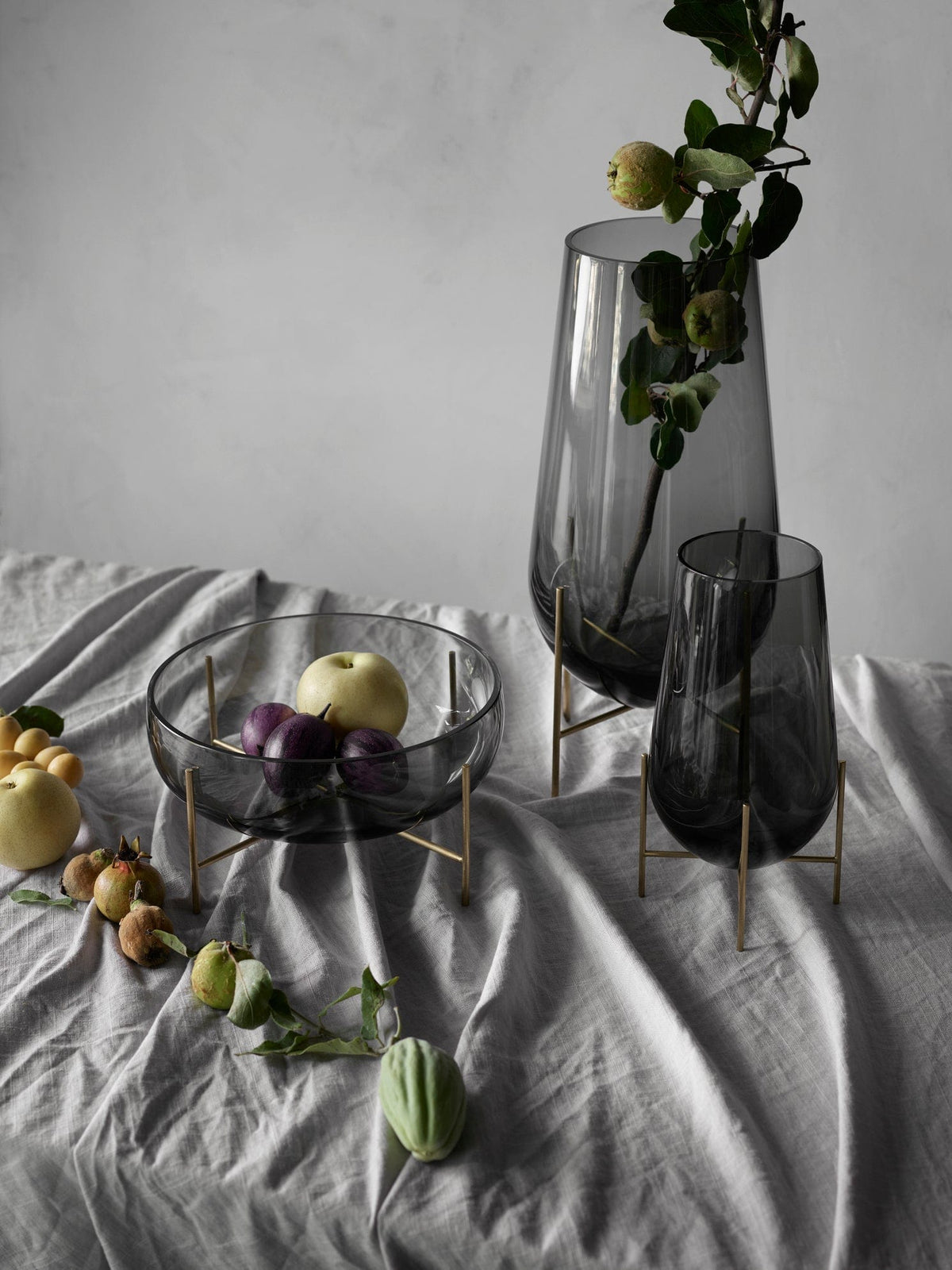 Echasse glass vases with fruit on draped cloth.