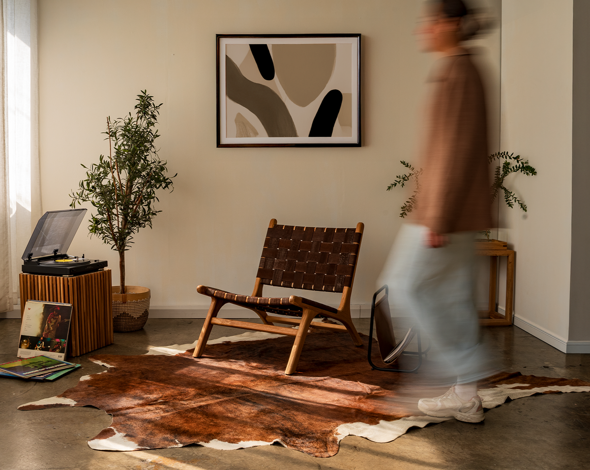 Person walking in a room with a vinyl record player, armchair, and abstract art on the wall.