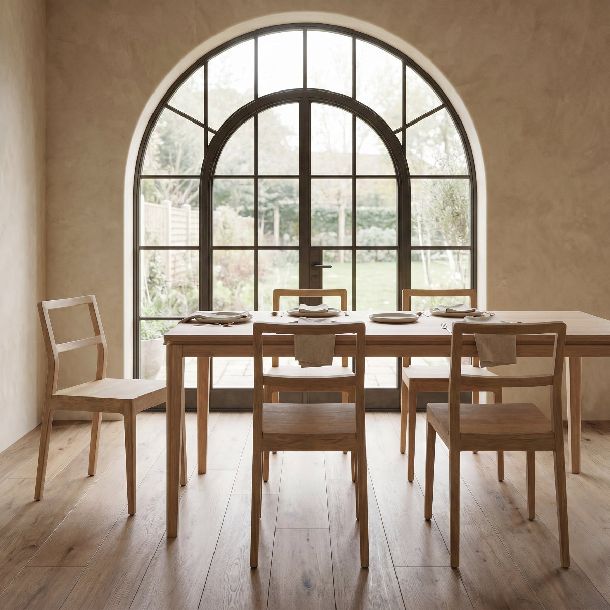 Dining area with wooden table and chairs in front of a large arched window.