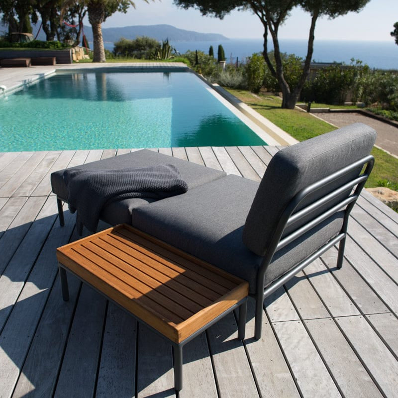Dark grey chair and ottoman with bamboo side table by pool.