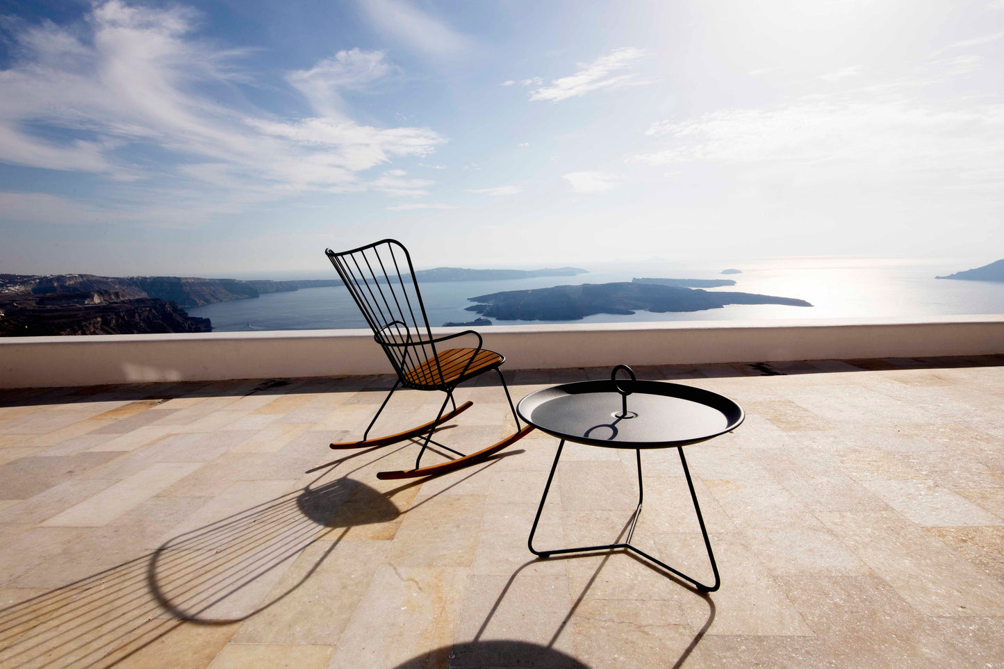 Black EYELET rocking chair and table on a terrace overlooking the sea.