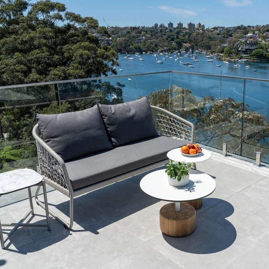 Outdoor patio set with gray cushions on a balcony overlooking a waterfront view.