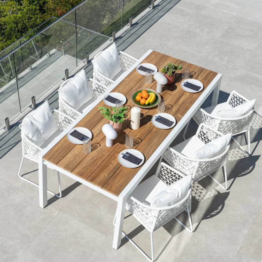 Outdoor dining setup with a wooden table and white chairs on a rooftop terrace.