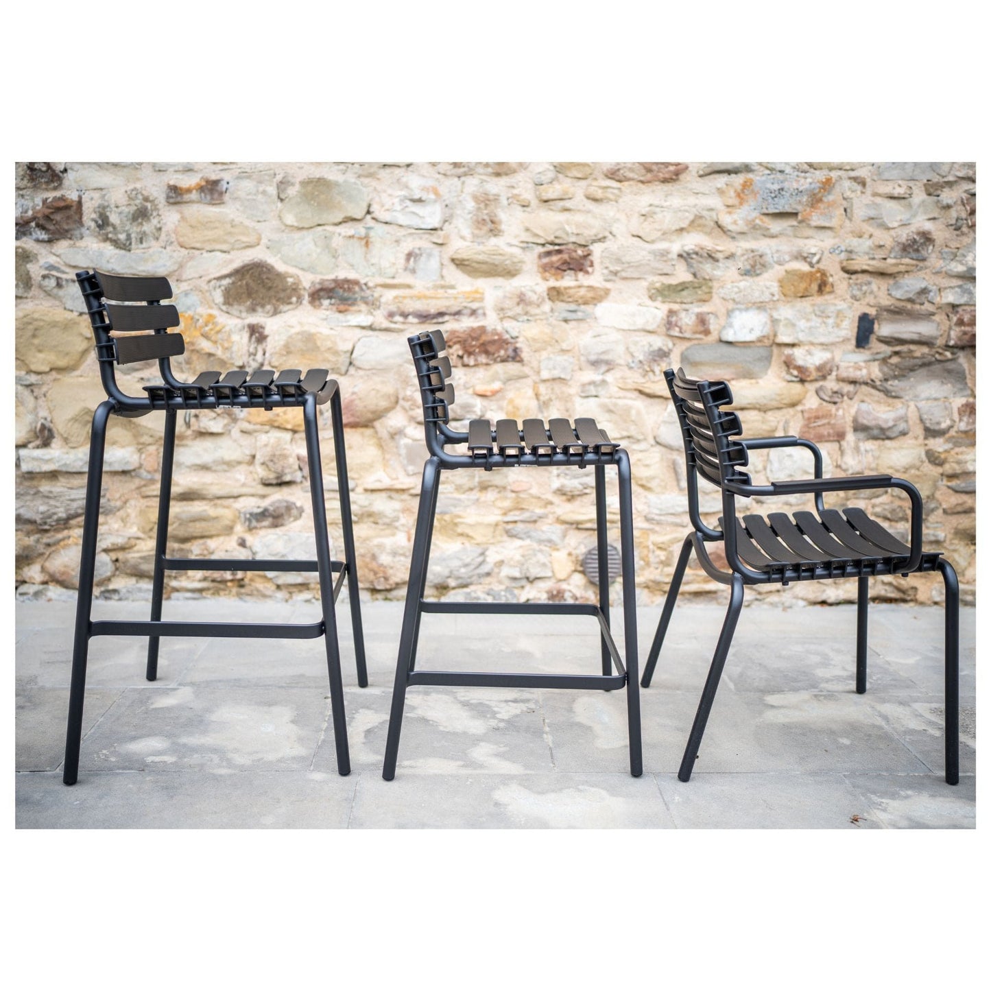 Black relipsc counter chairs against stone wall