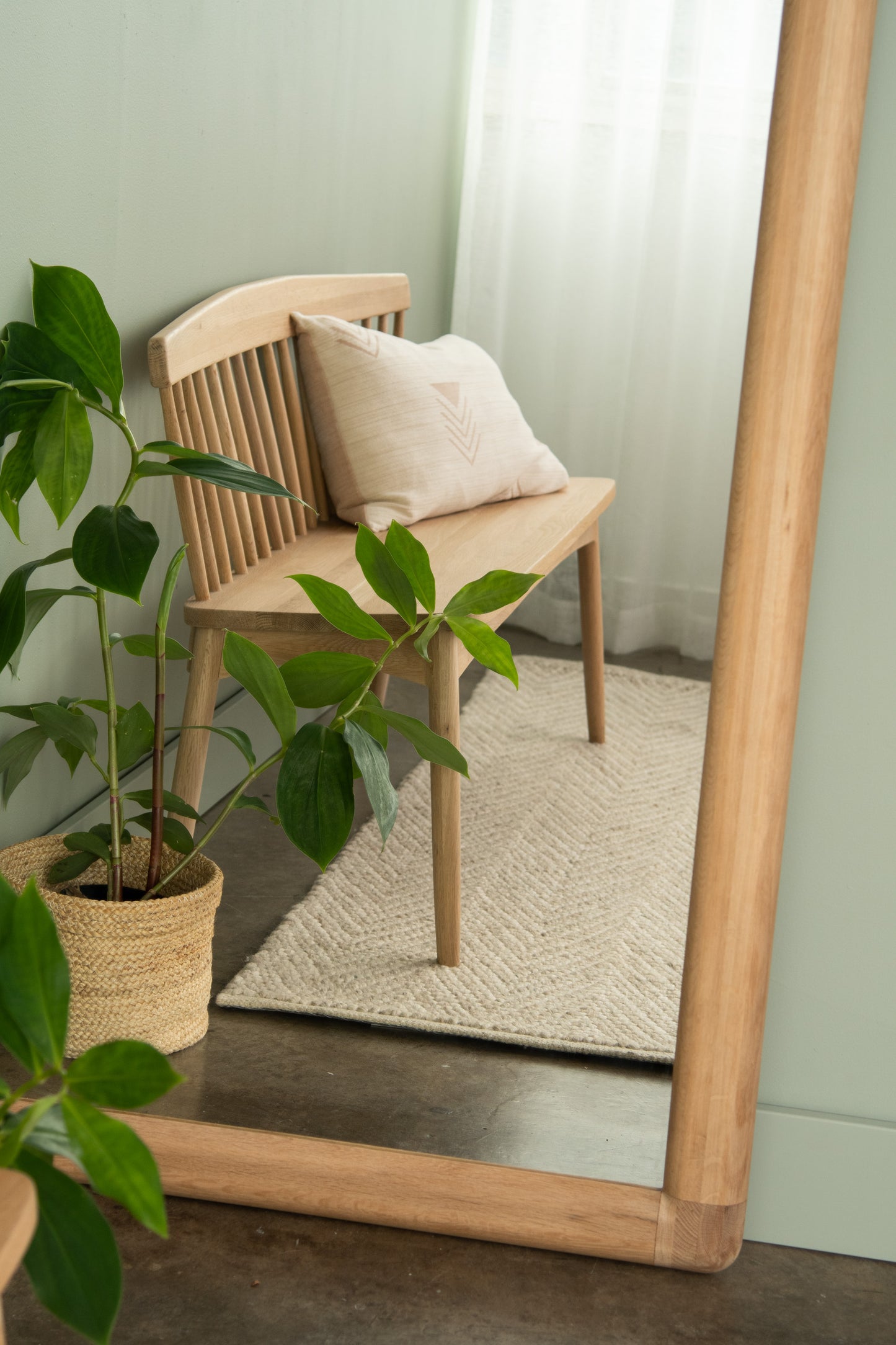 Wooden bench with pillow, rug, and houseplant near mirror.