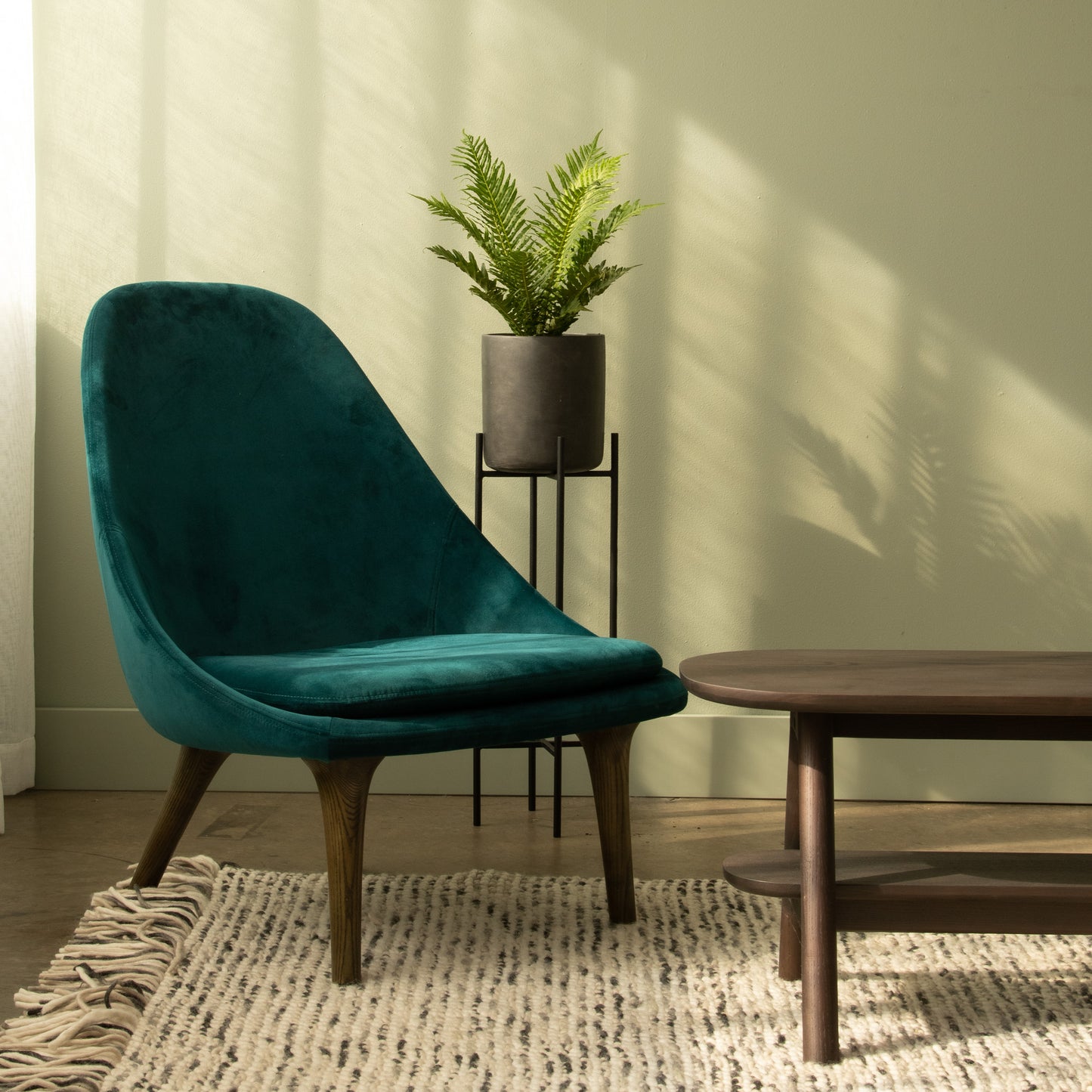 Teal velvet chair, plant, and wooden table in room