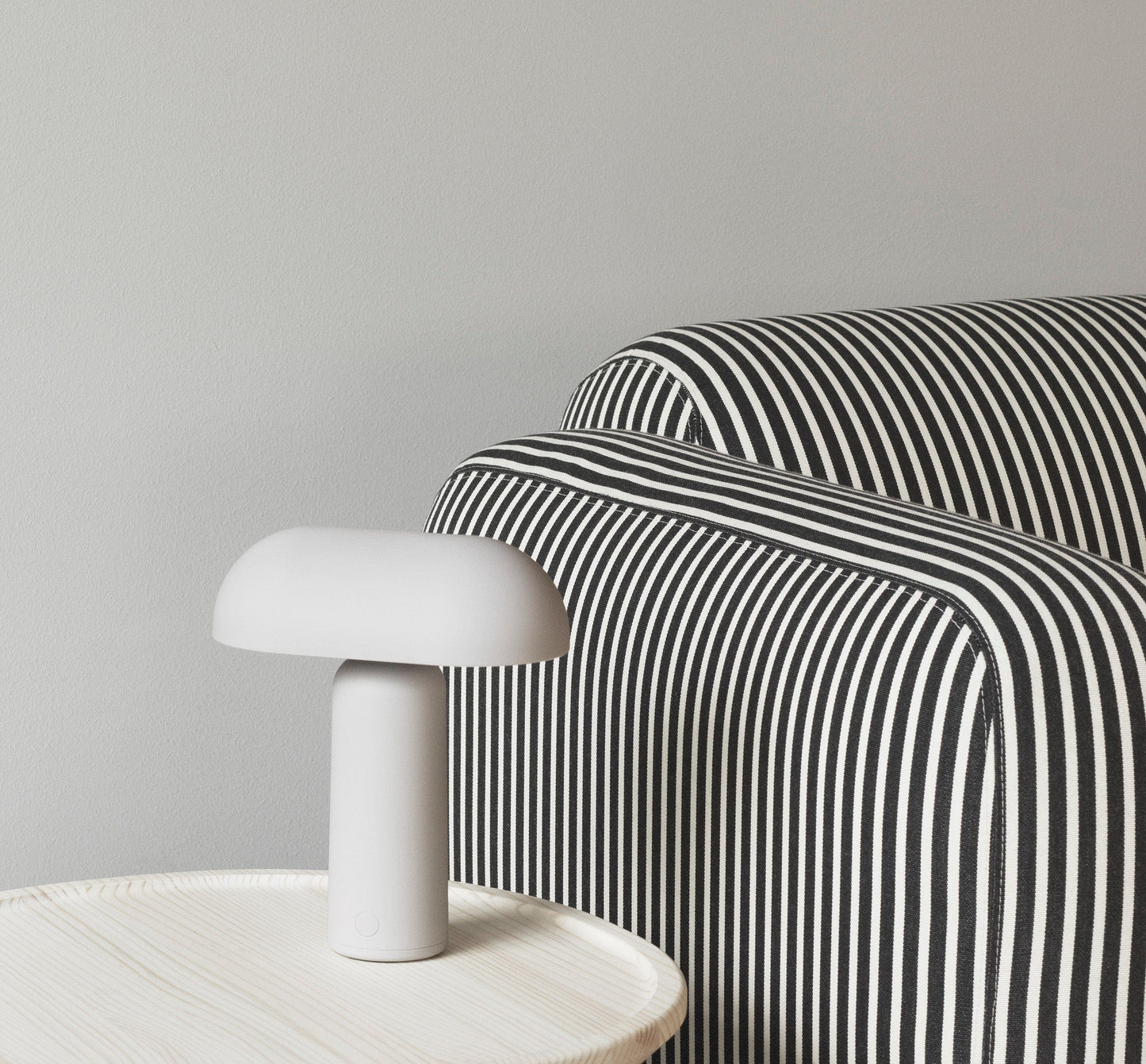 Gray table lamp on side table next to striped armchair.