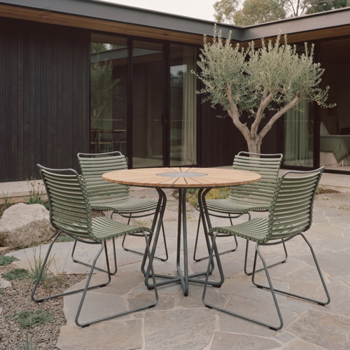 A 5-piece outdoor patio dining set consisting of a round wooden-top table with a metal base and four matching slatted metal chairs, set on a stone patio in front of a modern house.