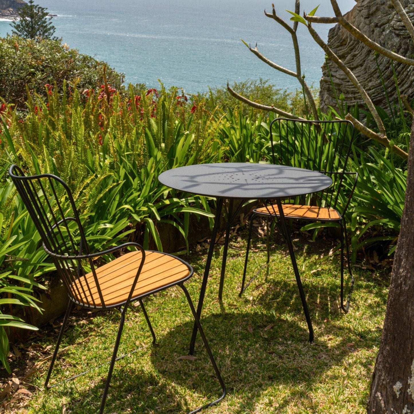 Table and chairs on grass, ocean in background.