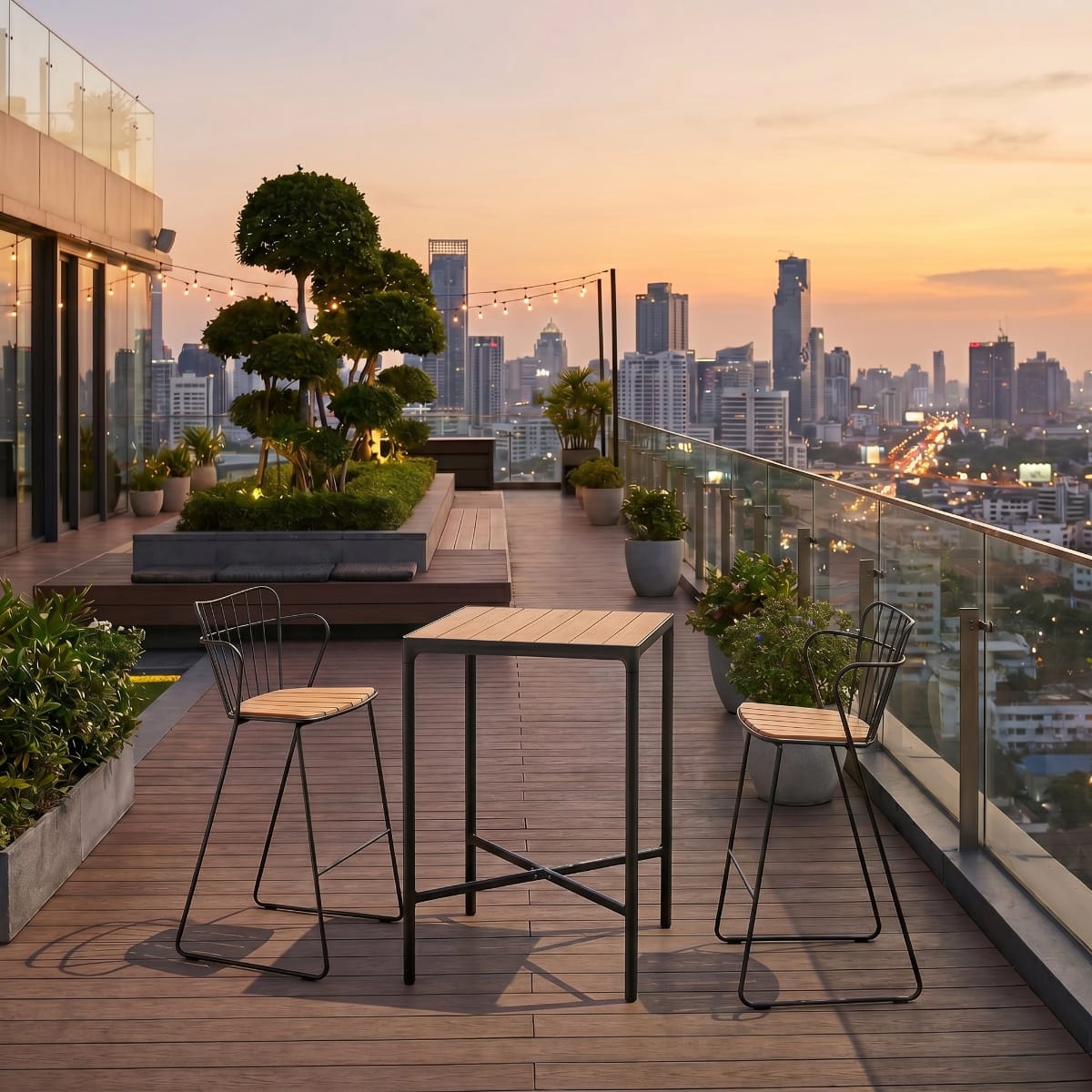 Outdoor rooftop terrace with table and chairs overlooking a city skyline at sunset.