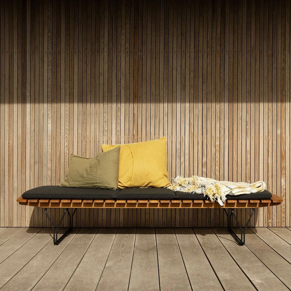 Wooden bench with pillows and blanket.
