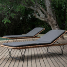 Two outdoor chaise lounge chairs on a wooden deck.