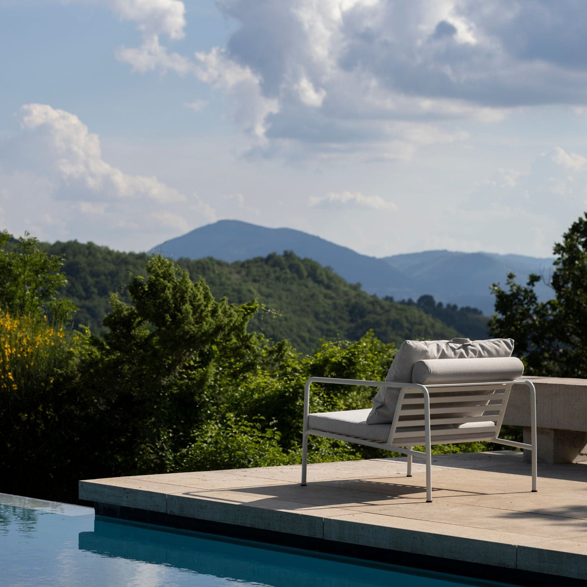 Lounge chair on a patio overlooking mountains and a pool.