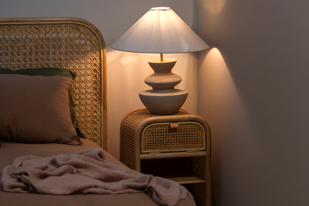 Wicker nightstand with lamp and bed in a dimly lit room