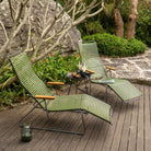 Two green chaise lounge chairs on a wooden deck.