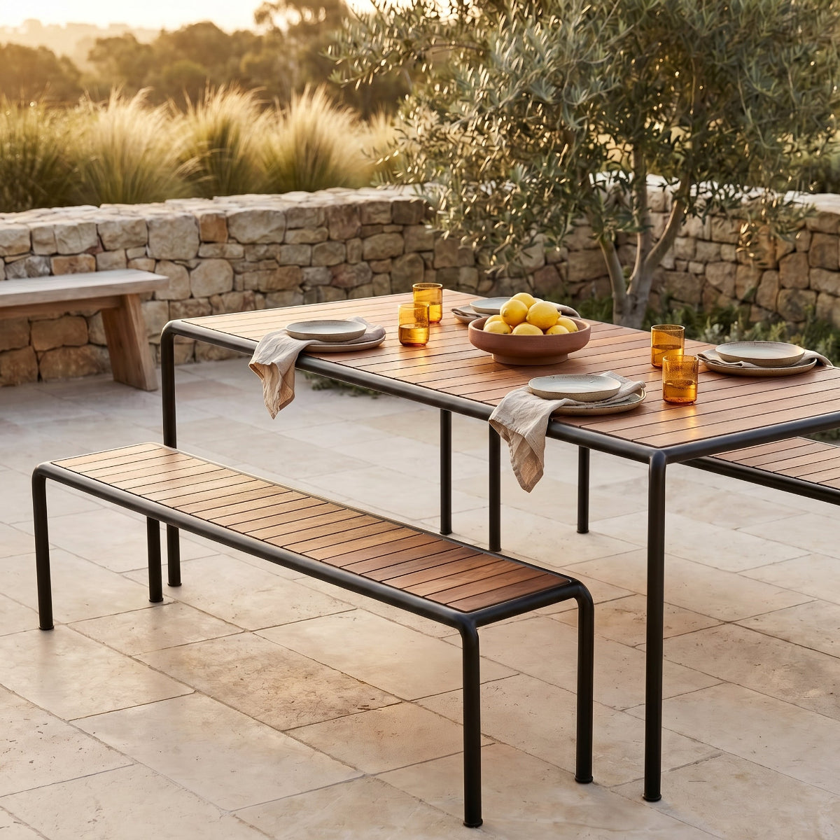 Outdoor dining table with benches and a stone wall in the background
