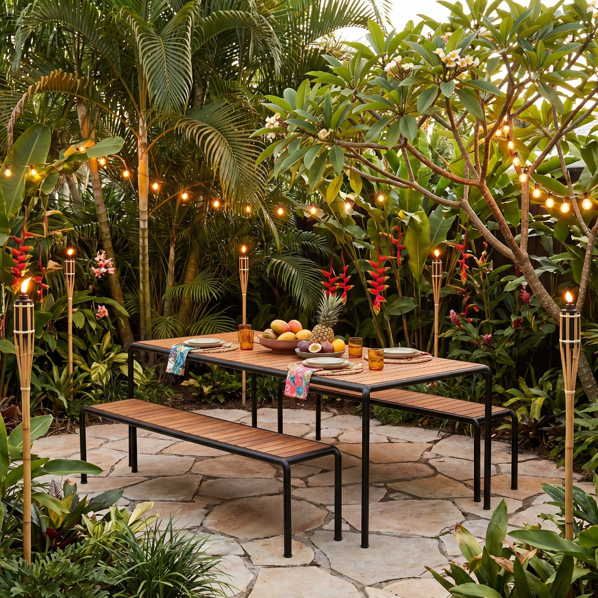 Outdoor patio setting with a table, benches, and decorative lights in a tropical garden.