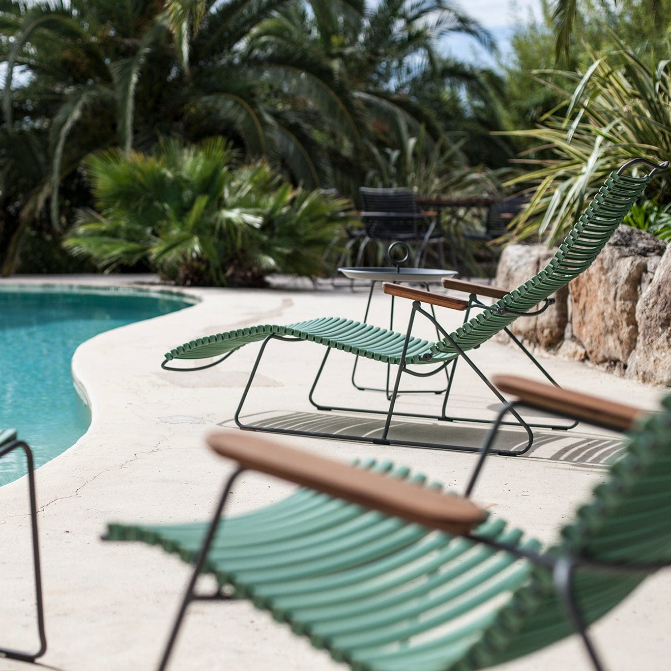 Poolside area with green lounge chairs and a table in a tropical setting.