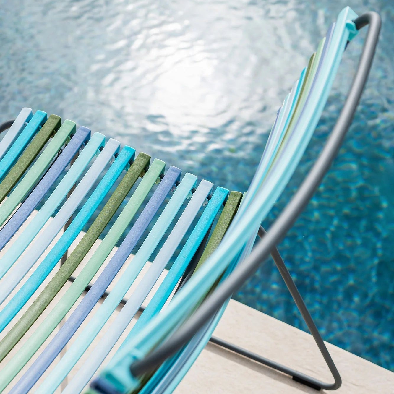 Colorful striped chair by a pool with clear blue water.