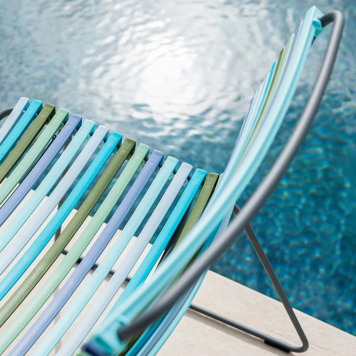 Colorful striped chair by a pool with clear blue water.