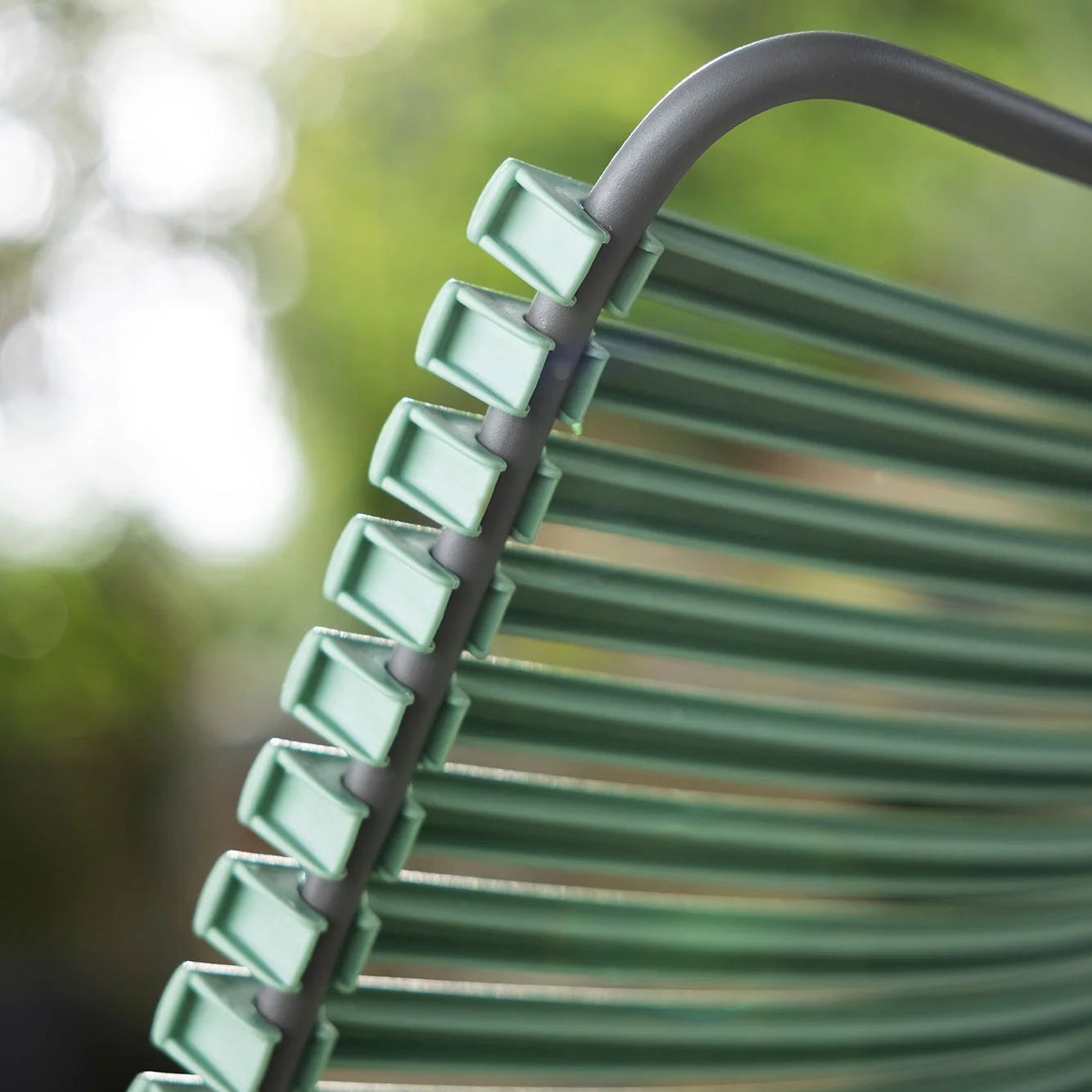 Close-up of a green metal chair with blurred greenery in the background