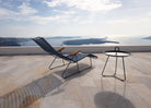 Black HOUE CLICK sunlounger and side table on a terrace overlooking the sea.