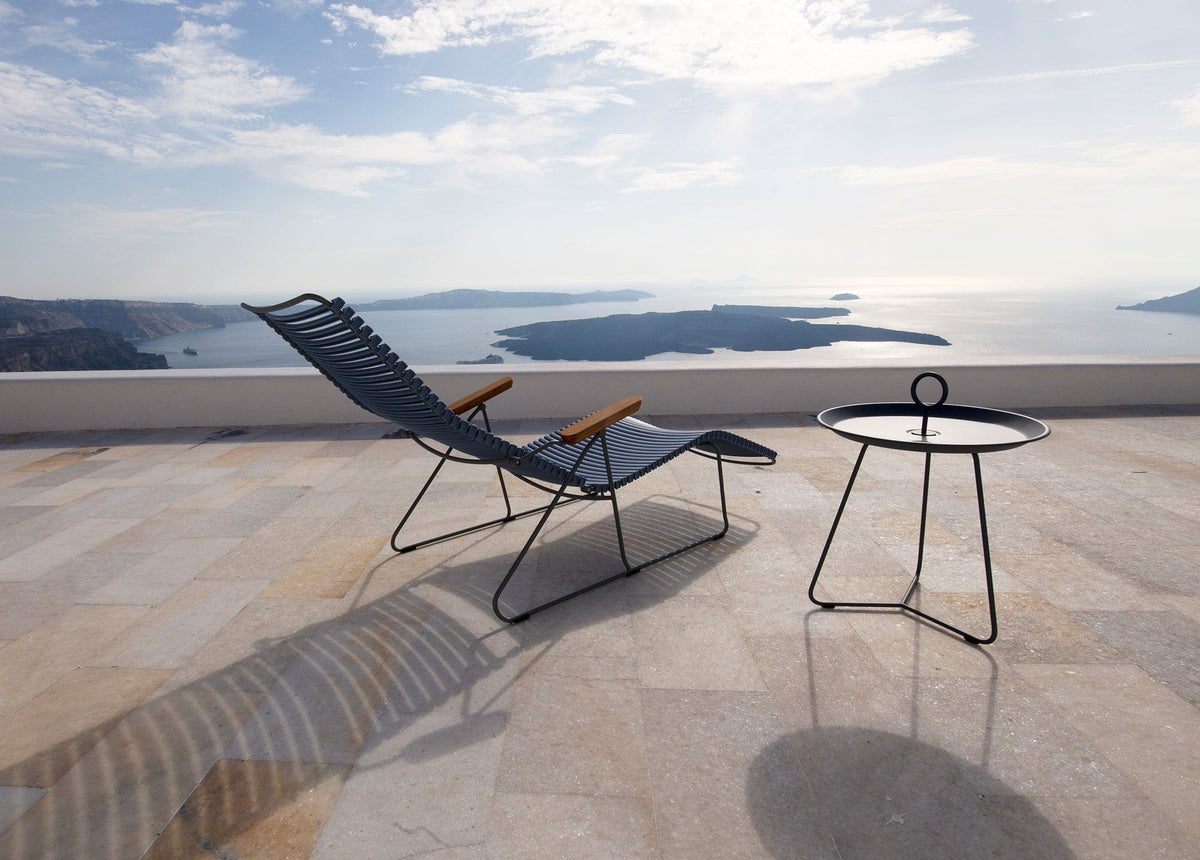 Black HOUE CLICK sunlounger and side table on a terrace overlooking the sea.