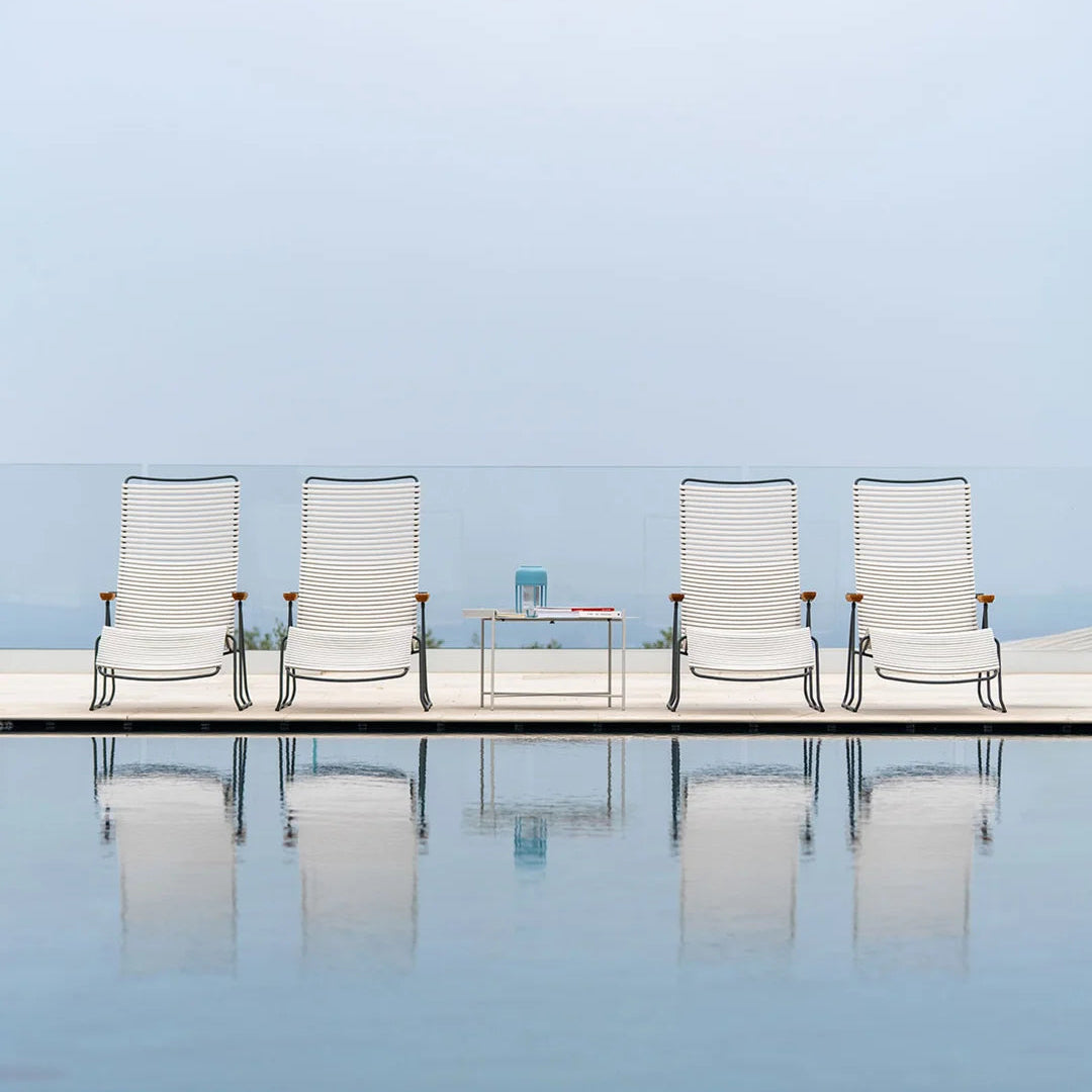 Four white chairs with black frames arranged around a small table by a pool with a clear blue sky.