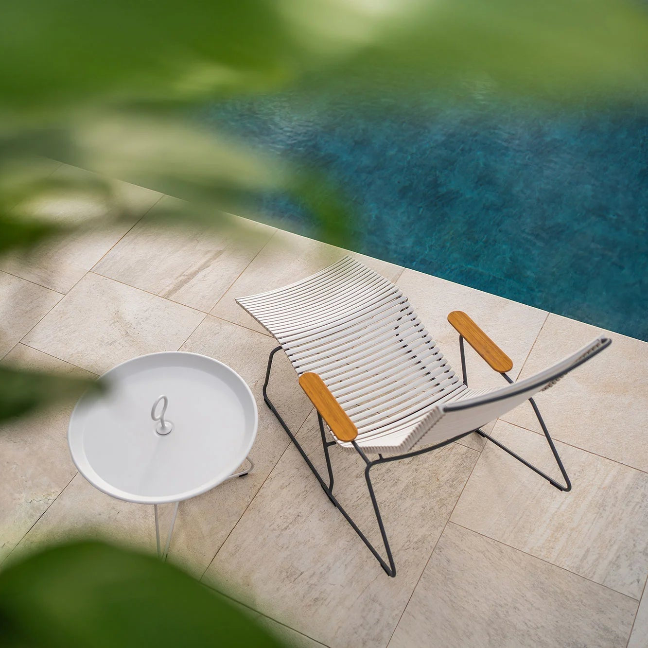 Chair and round table by a pool with greenery around