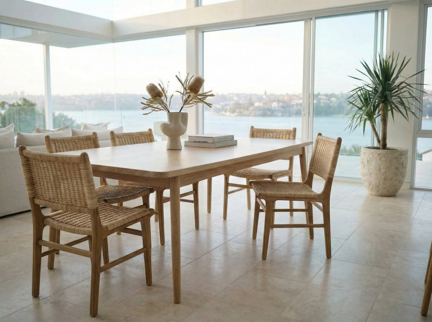 Dining area with wooden table and chairs near large windows with a view of water.