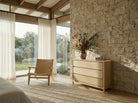 Modern bedroom with wooden dresser, chair, and stone wall.