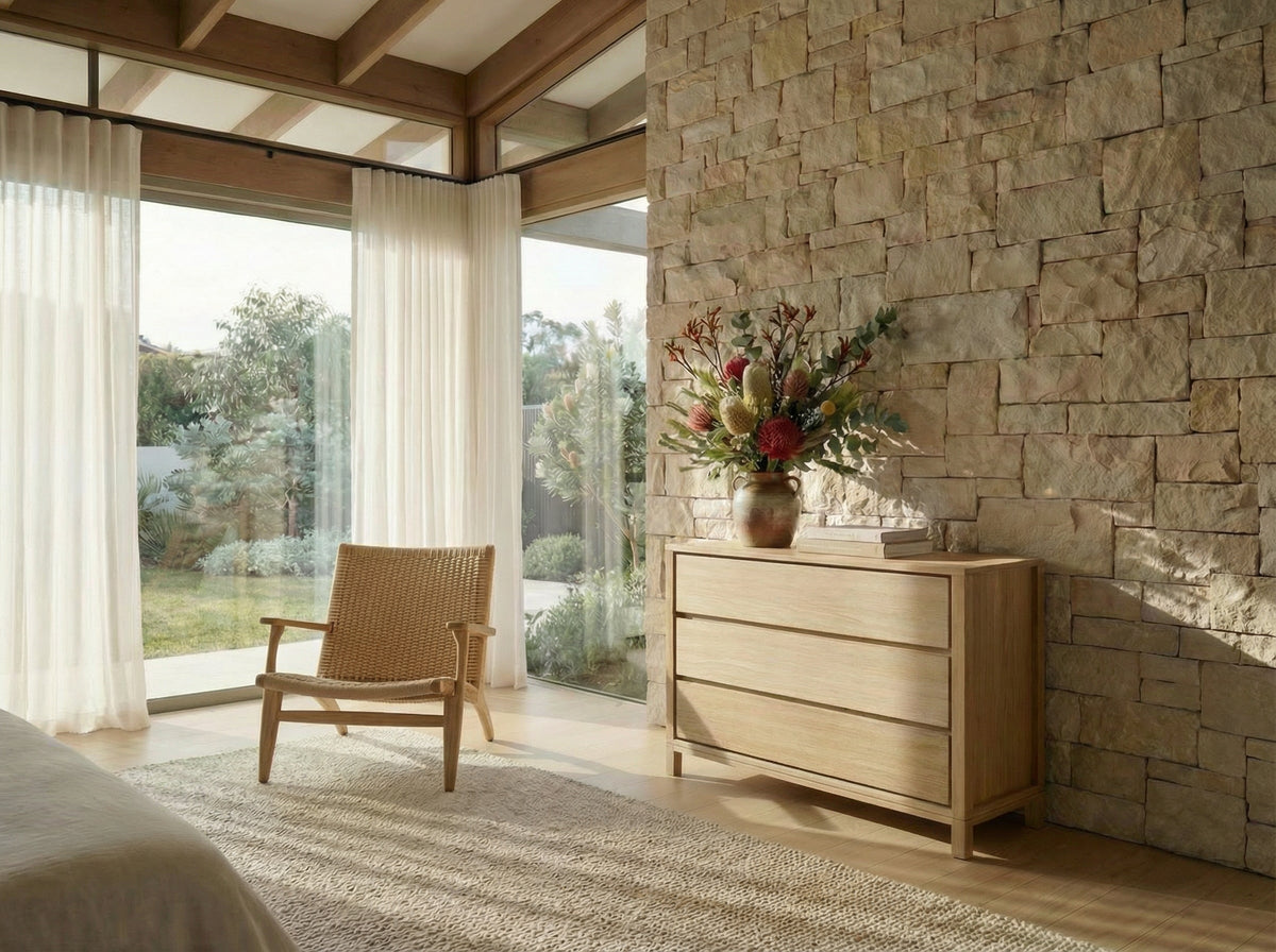 Modern bedroom with wooden dresser, chair, and stone wall.
