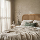 Neatly made bed with beige bedding and a wooden headboard in a softly lit bedroom.