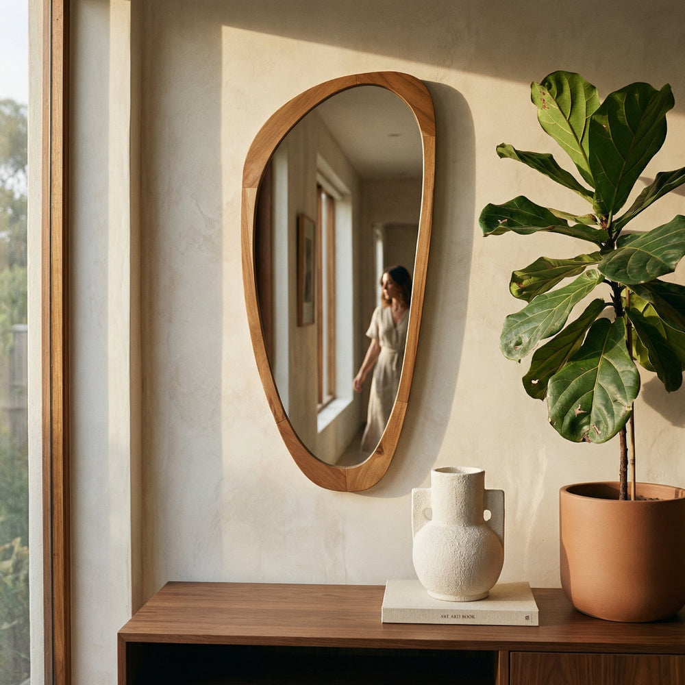 Oval wooden mirror on a wall with a plant and decorative items below.