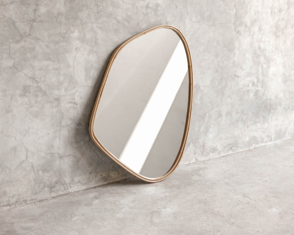 ELE125 Mirror with organic shape and gold frame against concrete wall.